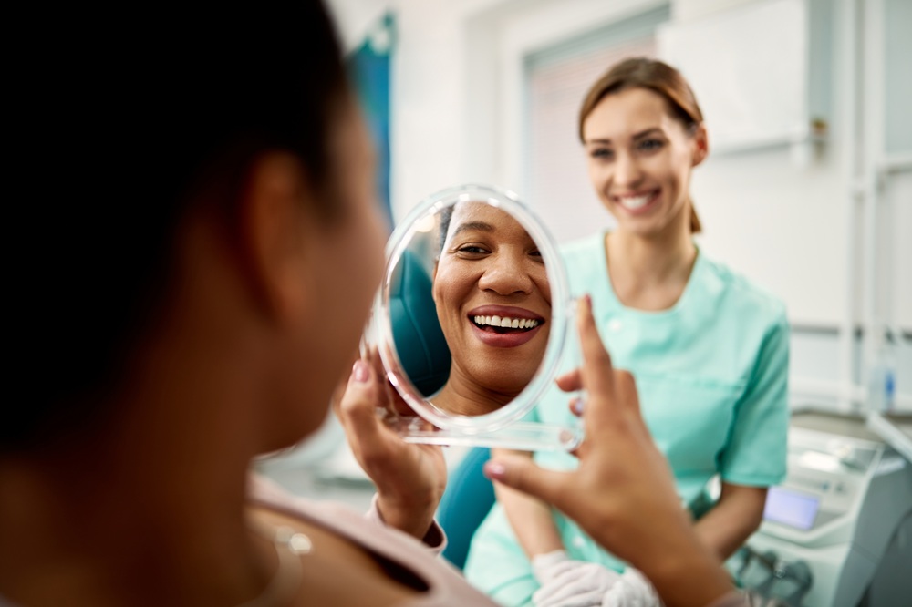 Patient holding a mirror and smiling at clean, polished teeth while dental professional stands nearby, showcasing results from San Diego teeth cleaning - San Diego Teeth Cleaning