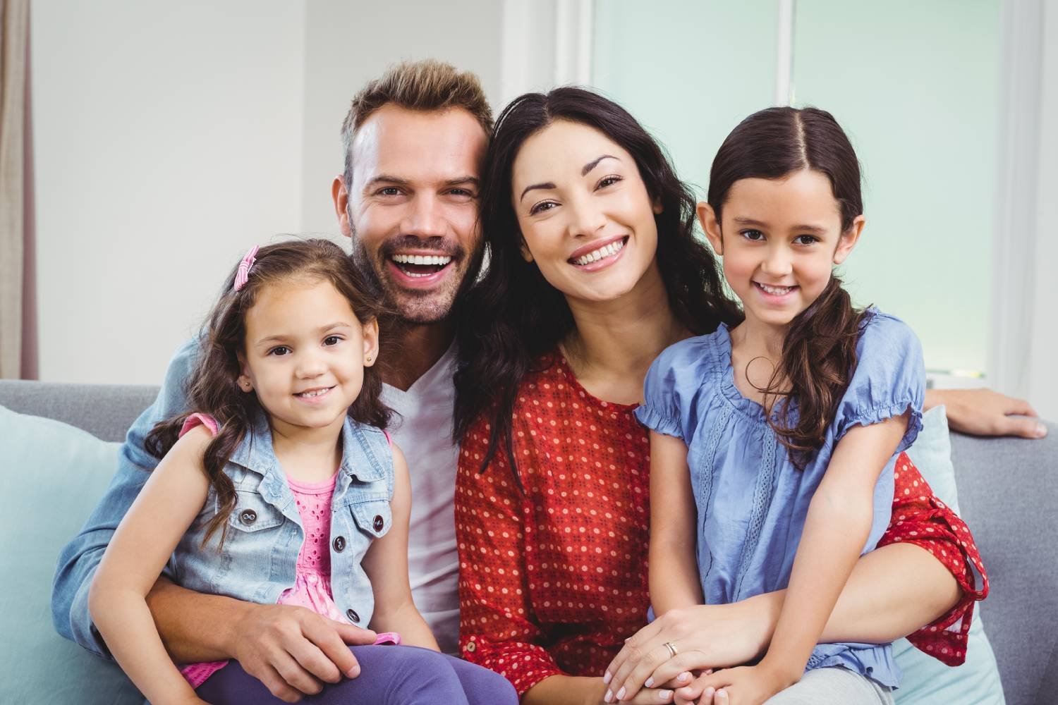 Portrait of cheerful parents sitting with daughters on sofa at home