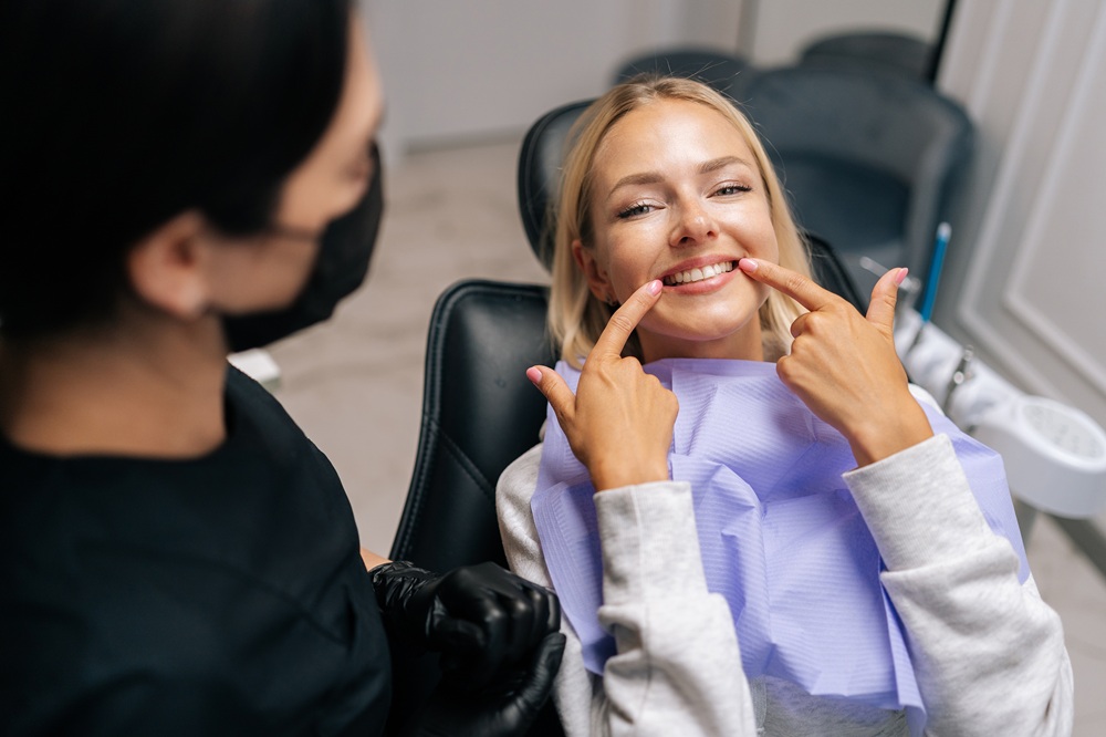 Smiling female patient in dental chair pointing to her teeth after a cleaning, highlighting fresh and polished results from San Diego teeth cleaning - San Diego Teeth Cleaning